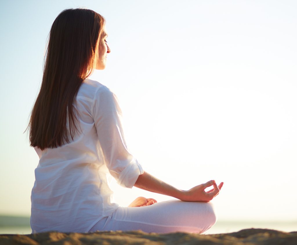 Side view of meditating woman sitting in pose of lotus against clear sky outdoors